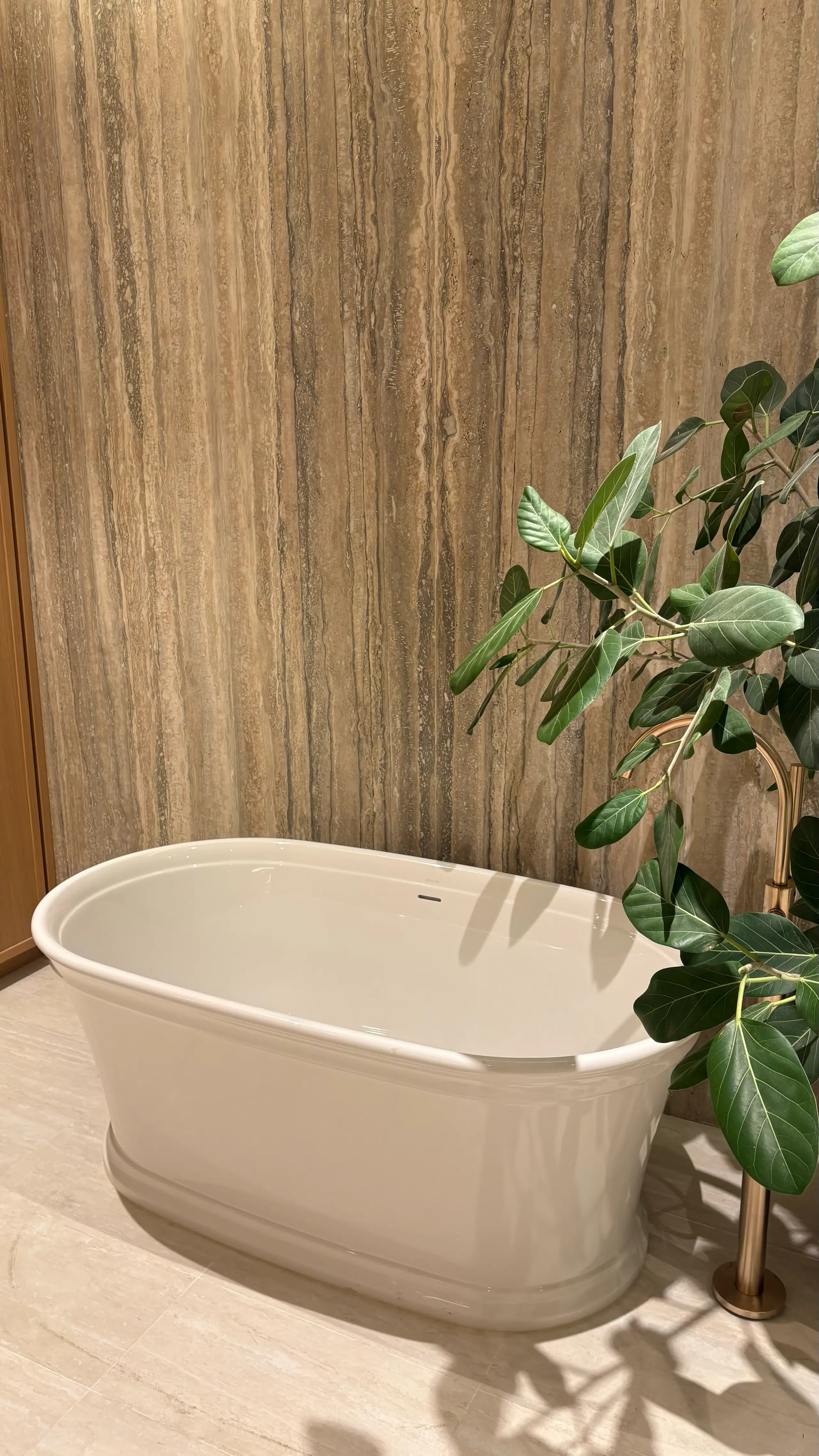 Freestanding tub against a book-matched travertine wall, lit from a cove above