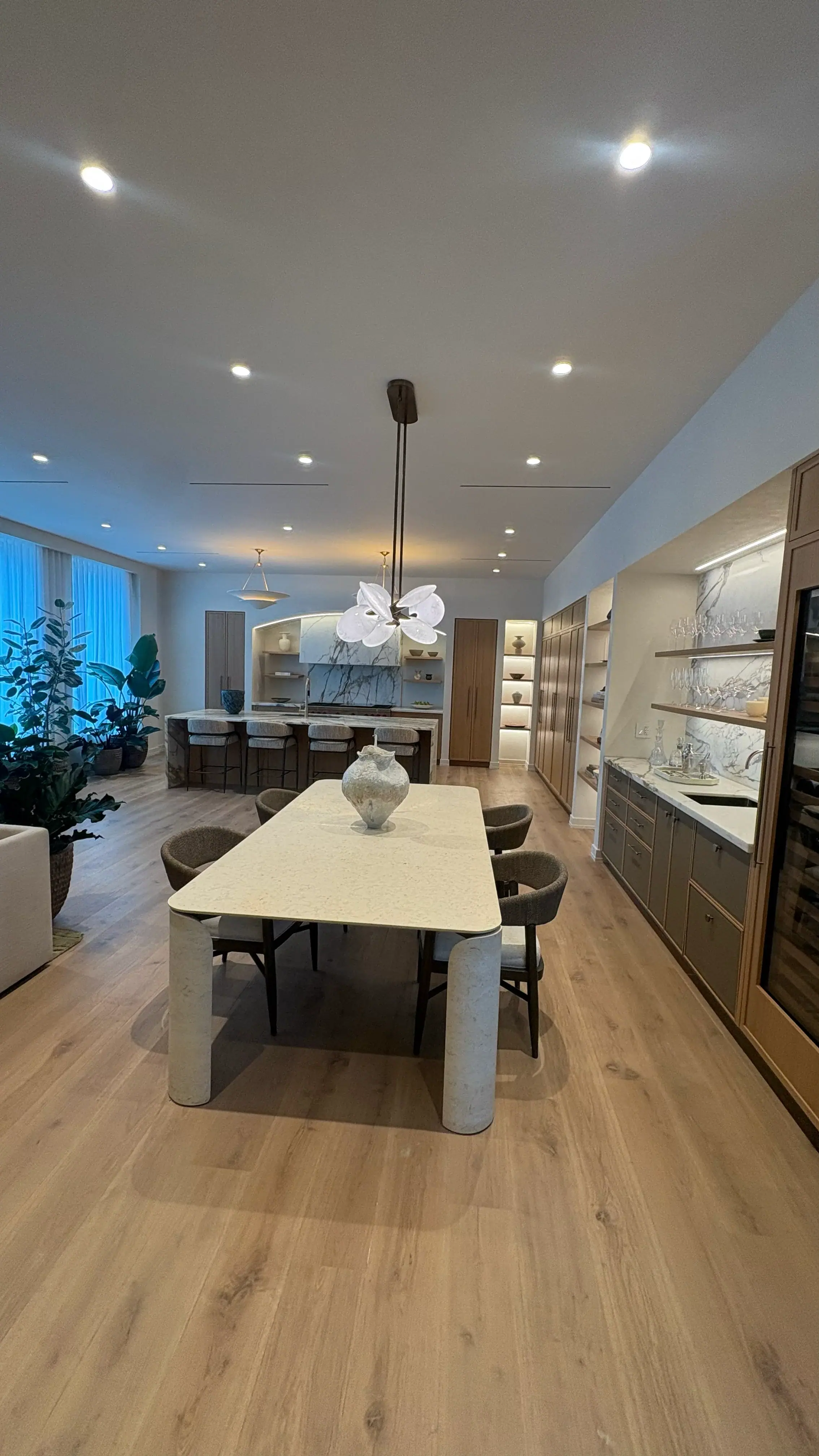 Open-plan dining with a sculptural chandelier and a lit bar wall beyond