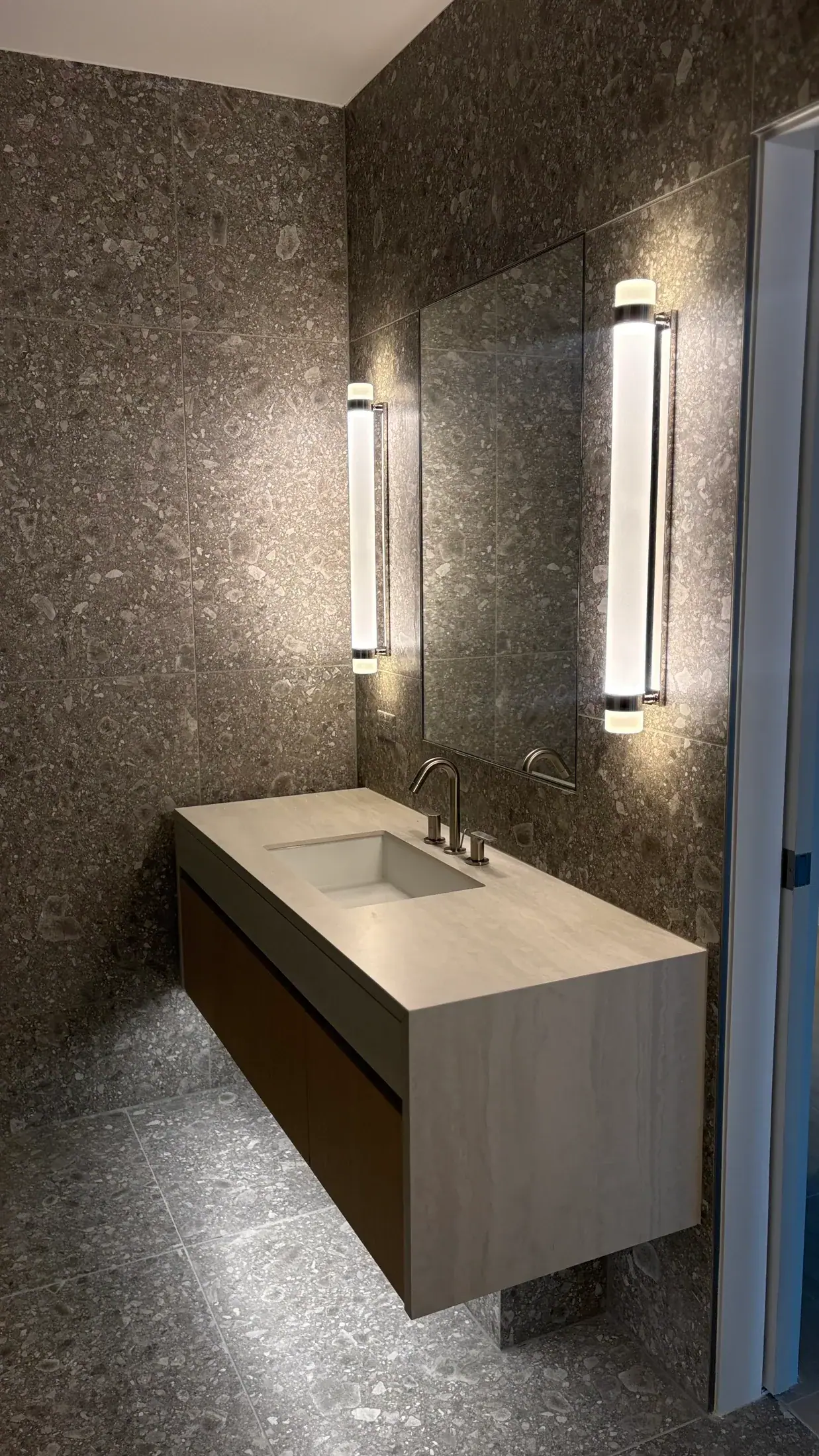 Floating vanity in veined stone with vertical lights beside the mirror