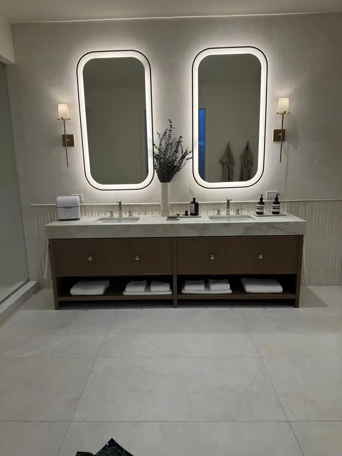 Double vanity with backlit oval mirrors and sconces between them